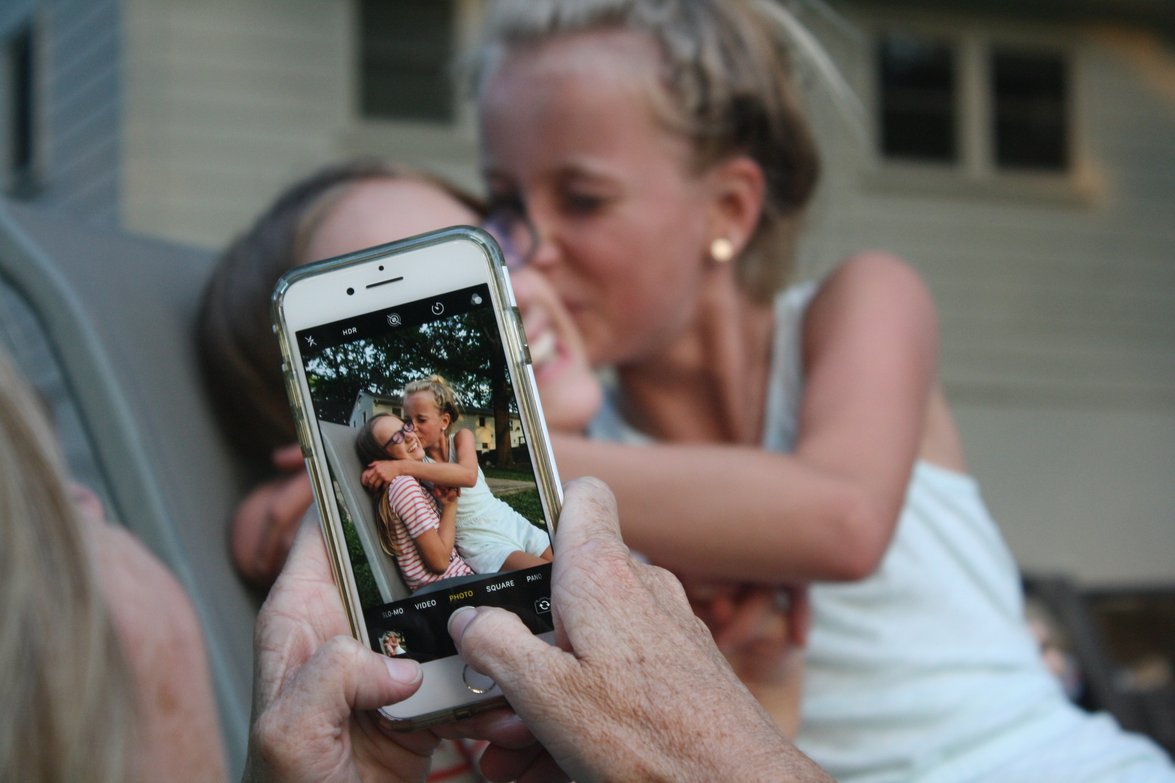 A woman photographs her mother and daughter with a smartphone. Indicating how the benefit of capturing a precious memory is more important than the smartphone's features.